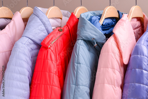 New collection of down jackets on hangers in the market. Colorful background of modern spring, autumn outerwear.