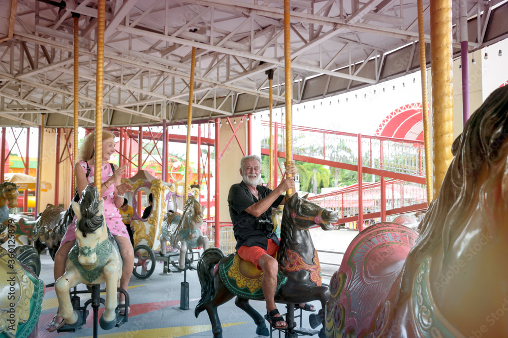 Elderly couple spending time together at theme park on weekend, senior people hanging out and having fun at amusement park. Grandpa and grandma enjoying at carousel spinning