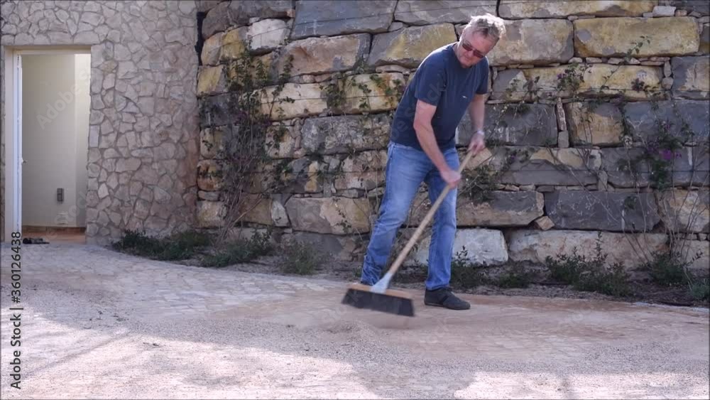 Man sweeping up dirt and gravel from his driveway Man sweeping up dirt and gravel from his driveway