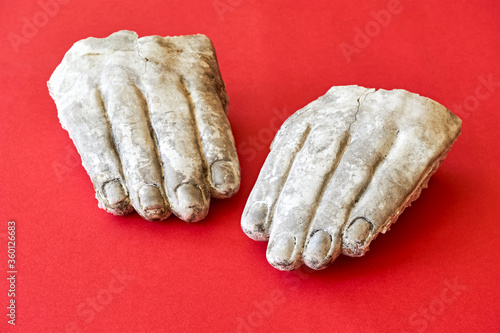 Photos Two white weathered broken hands of a stone statue on a red background