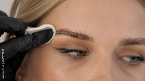 Professional master eyebrow woman removes liquid on the eyebrows with a cotton swab in a beauty salon. Permanent makeup for eyebrows. Eyebrow lamination and styling