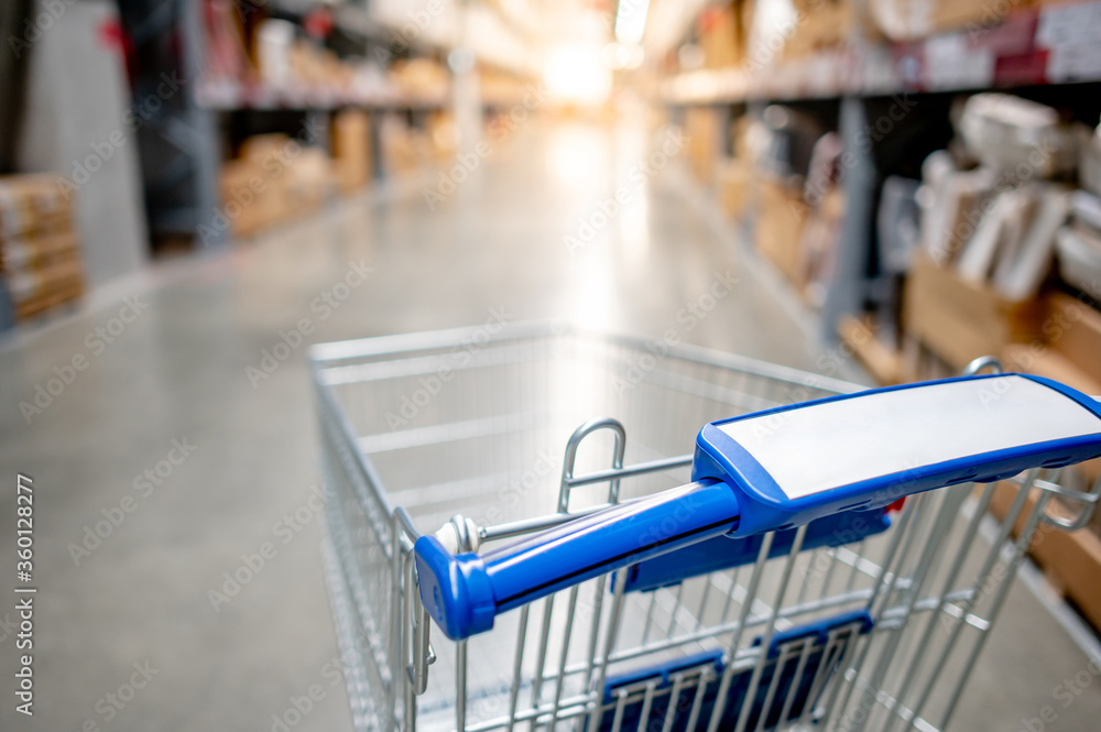 Empty shopping cart or shopping trolley in aisle of supermarket or grocery store. Buying concept Empty shopping cart or shopping trolley in aisle of supermarket or grocery store. Buying concept