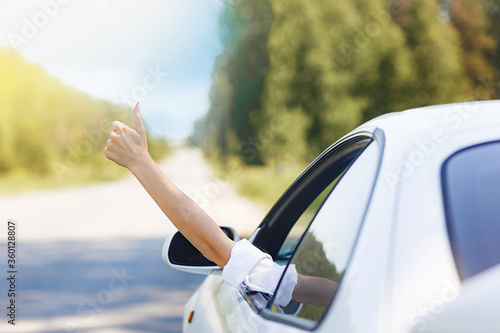 woman showing thumbs up/making Like / Ok sign with hand from car window with sunset sky, relaxing, enjoying road trip and feeling the air and freedom. Toward adventure, vacation