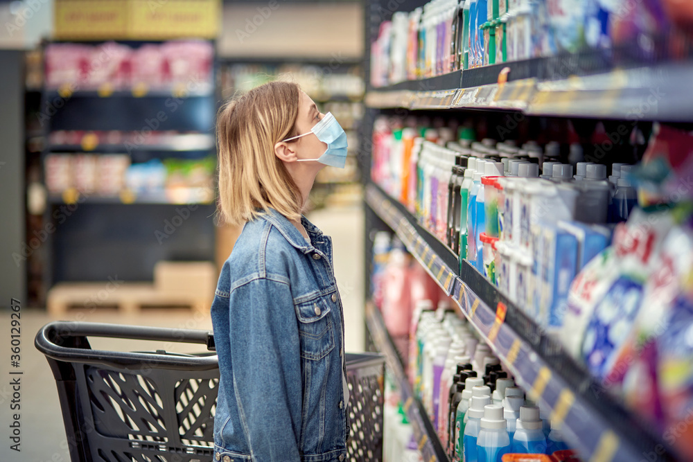 Girl in a shopping center in mask stands near a rack with household chemicals.