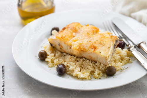 fried cod fish with cous cous and olives on white plate