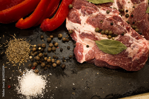 Juicy raw meat with vegetables and seasonings on a black background. Composition of meat. The process of preparing a meat dish.