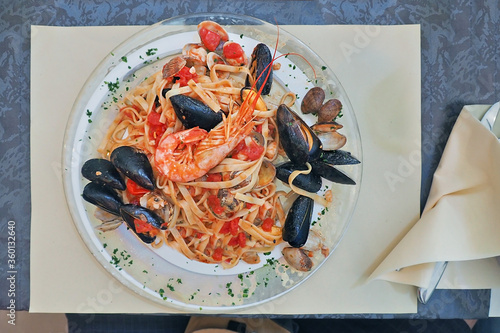 lifestyle shot eating italian style spaghetti seafood in tomato sauce served on clear glass plate dish in traditional local italy restaurant