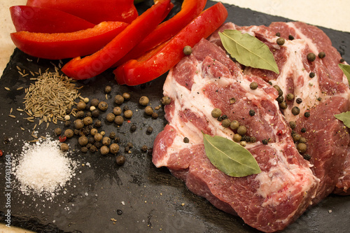 Juicy raw meat with vegetables and seasonings on a black background. Composition of meat. The process of preparing a meat dish.