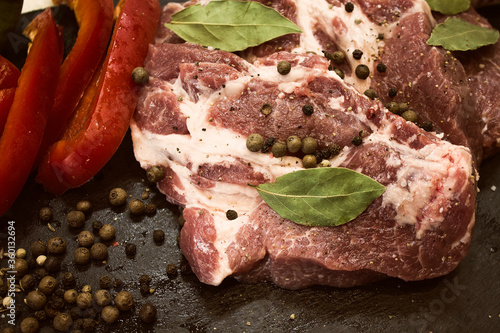 Juicy raw meat with vegetables and seasonings on a black background. Composition of meat. The process of preparing a meat dish.