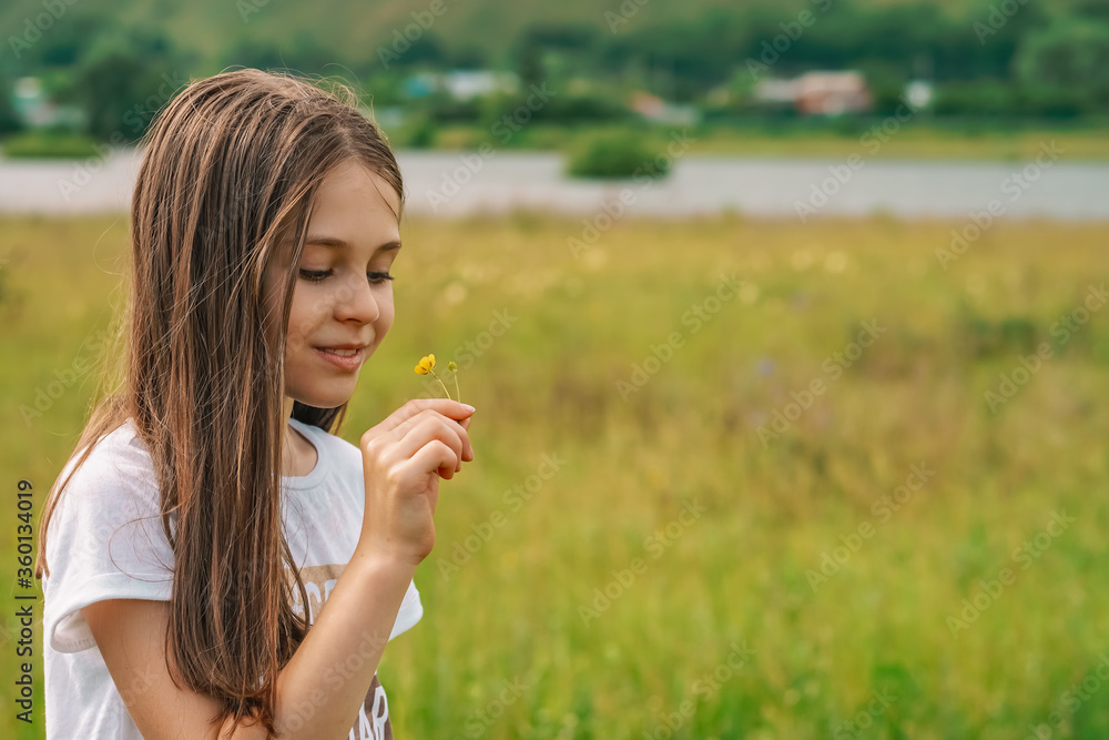 A little girl a child with long hair sniffs a wild flower in the countryside against the background of mountains an A little girl a child with long hair sniffs a wild flower in the countryside against the background of mountains an