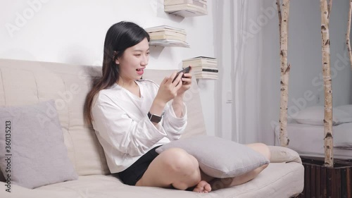 The beautiful woman sitting on the sofa uses her mobile phone to play games. photo