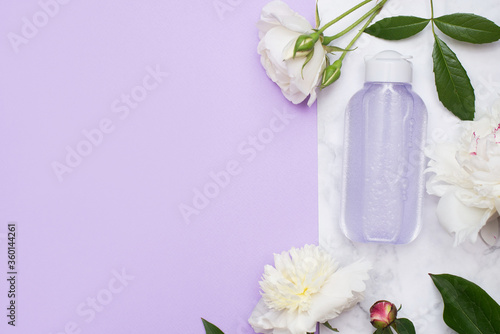 Cosmetic bottle with tonic or micelar water with flowers on marble background and pink copy space. photo