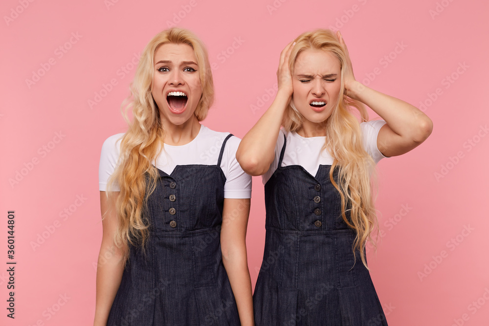 Indoor photo of young long haired blonde pretty woman closing her eyes and covering ears with raised hands while her sister shouting loudly, isolated over pink background Indoor photo of young long haired blonde pretty woman closing her eyes and covering ears with raised hands while her sister shouting loudly, isolated over pink background