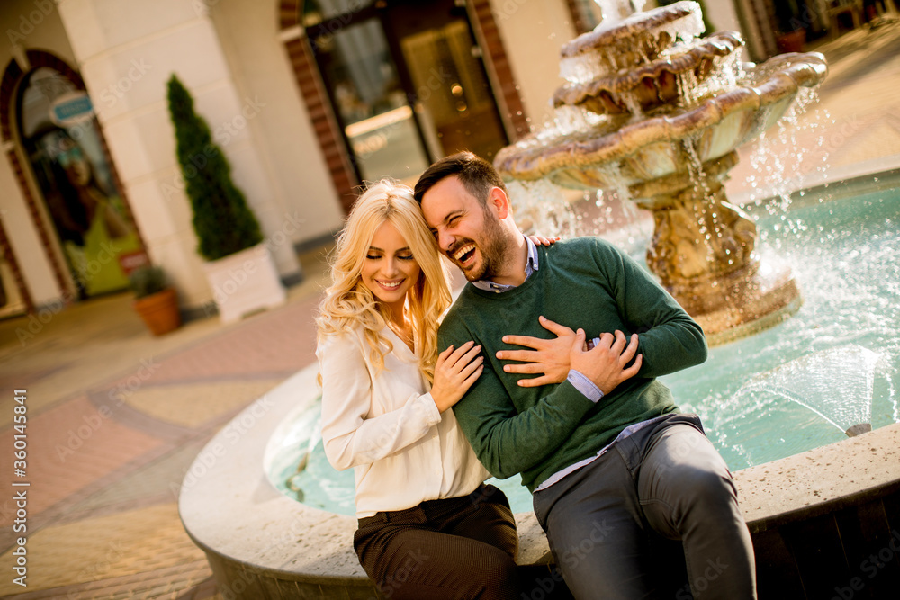 Beautiful smiling love couple sitting by the fountain on a sunny day Beautiful smiling love couple sitting by the fountain on a sunny day