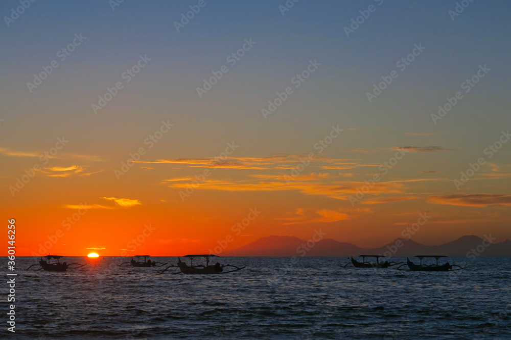 Fototapeta premium Vibrant colours beautiful ocean sunset with dark fishermen boats silhouettes at Kuta beach, Bali, Indonesia