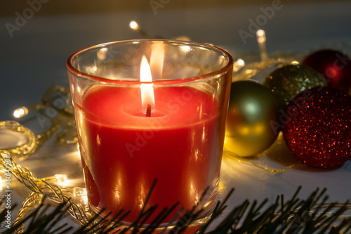 Red christmas candle, burning candle fire on a table with holiday garland and pine tree decorations and balls