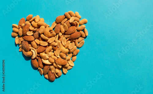 Various nuts forming heart shape on blue background with copy space. Top view. Different kind of tasty and healthy nuts, snack.