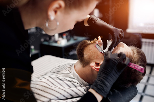 Barber shaving a man in barbershop, close up