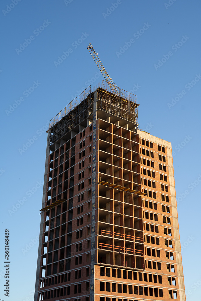 Fototapeta premium construction of a high-rise building against the blue sky, multi-storey building, red brick house