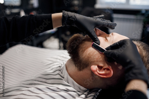 Barber shaving a man in barbershop, close up