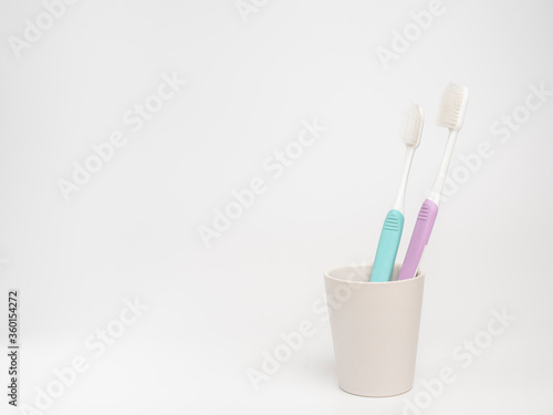 Old used pastel toothbrush in ceramic cup on white background.