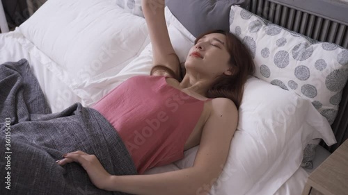 attractive asian woman wake up naturally in her bed, stretching body. lady sleeping in bedroom arousing by sunlight, looking up at the ceiling. genuine lifestyle