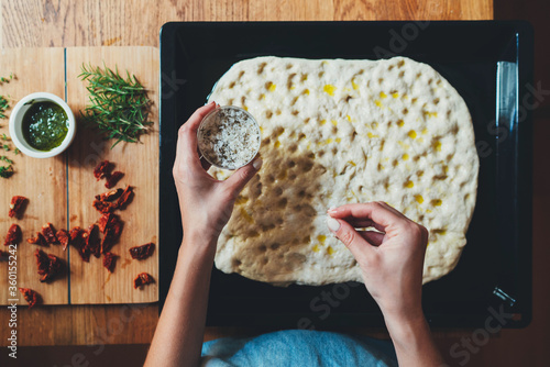 Top view of woman cooking italian focaccia adds ingredients to the dough, Italian focaccia with rosemary and sun-dried tomato, Homemade Food Concept, Cooking Class Online photo