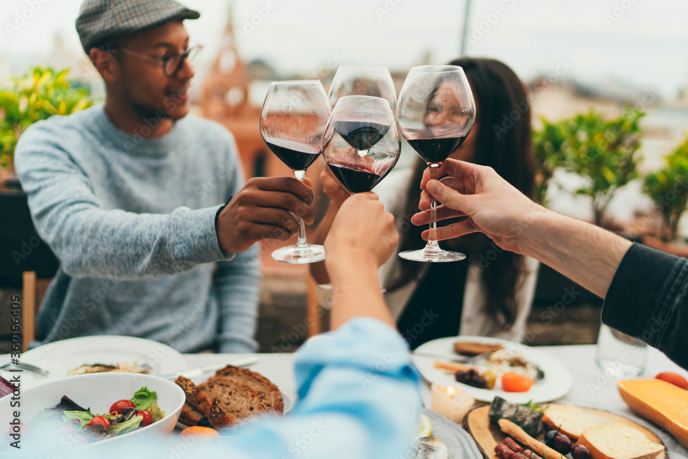 Young people celebrating together drinking red wine glasses on patio garden  at summer party. Diverse friends having fun cheering glasses during dinner  party. Friendship and celebration concept Stock Photo