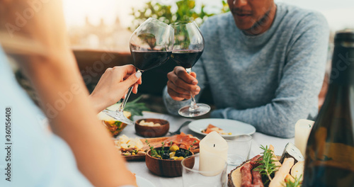 Couple enjoying romantic dinner at restaurant terrace drinking red wine and eating healthy mediterranean food, Lovely couple making cheers with red wine glasses at summer day at terrace