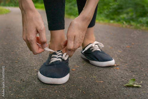 Close-up of women's hands tying shoelaces in dark blue sneakers on a jog in the woods.