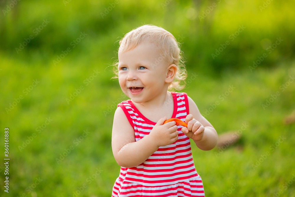 Cute little girl smiling in red summer dress walking on green lawn Cute little girl smiling in red summer dress walking on green lawn