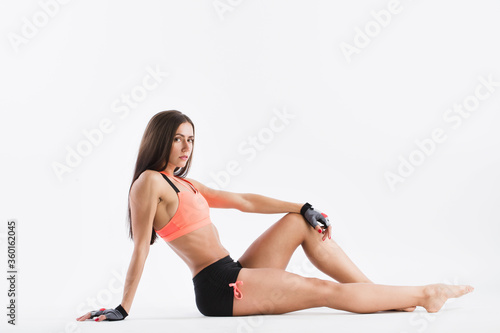 Beautiful fitness woman slim figure in sportswear posing in the studio. Sporty girl sitting on the floor in full.