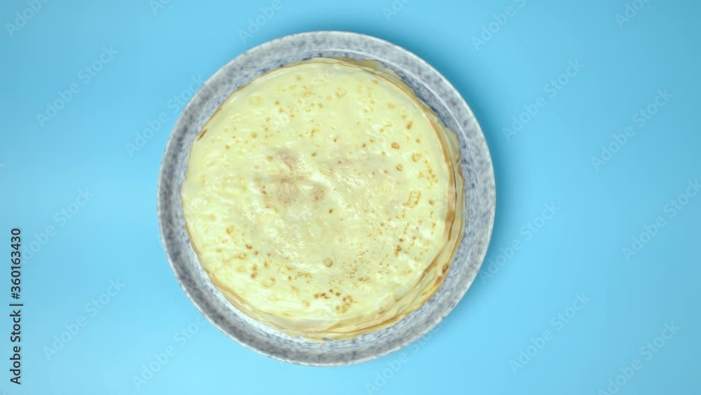 Top view of spinning French Crepes/Pancakes in a serving plate on a blue background Top view of spinning French Crepes/Pancakes in a serving plate on a blue background