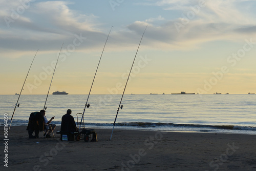 Sports fishermen with fishing rods at the beach of Katwijk aan Zee in the evening at sun set 