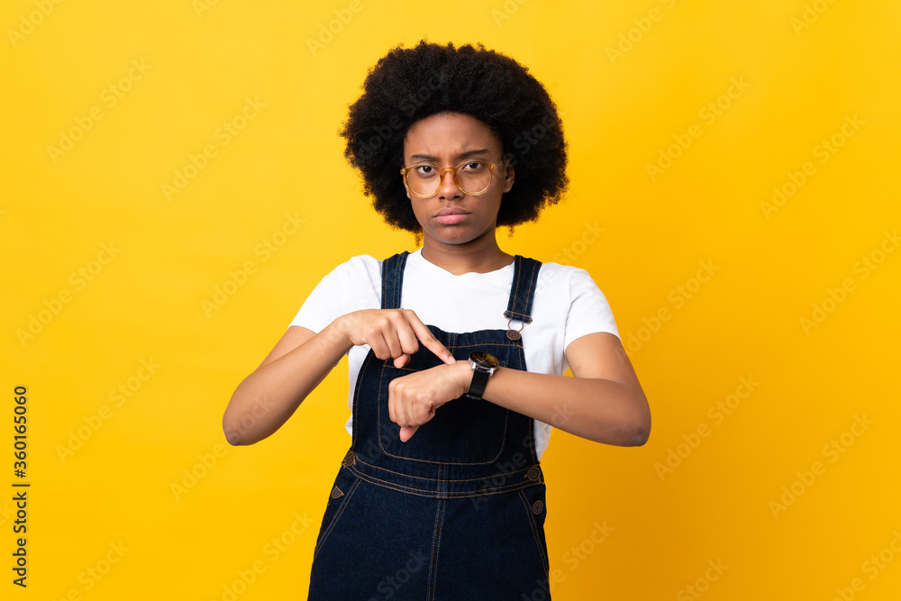 Young African American woman isolated on yellow background making the gesture of being late Young African American woman isolated on yellow background making the gesture of being late