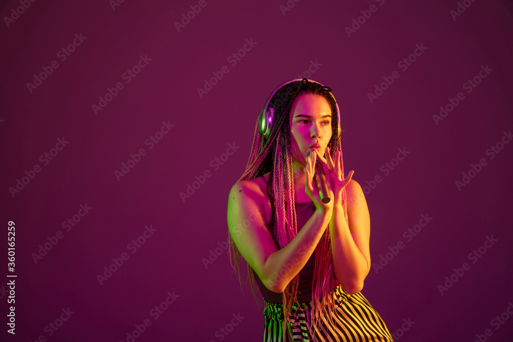 Singing with headphones, speaker. Young caucasian woman on pink studio background in neon light. Beautiful model with dreadlocks. Human emotions, facial expression, sales, ad concept. Freak's culture. Singing with headphones, speaker. Young caucasian woman on pink studio background in neon light. Beautiful model with dreadlocks. Human emotions, facial expression, sales, ad concept. Freak's culture.