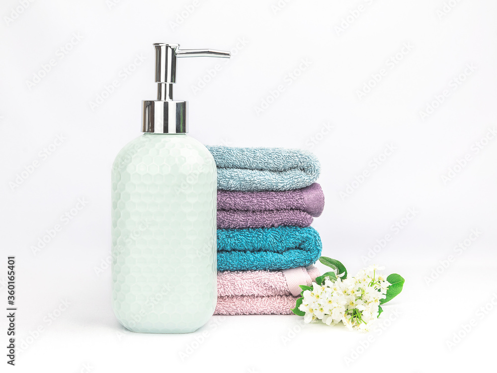 Light turquoise ceramic soap dispenser with multicolored soft towels and fresh flowers on a white background. Bathroom wellness spa concept Light turquoise ceramic soap dispenser with multicolored soft towels and fresh flowers on a white background. Bathroom wellness spa concept