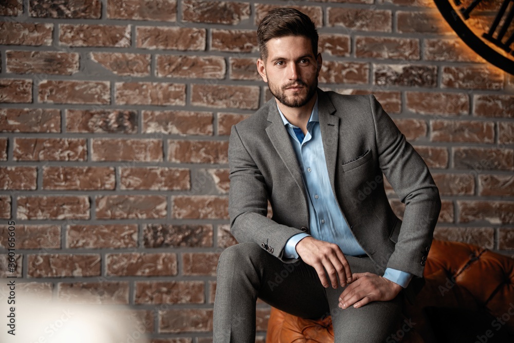 Cool and handsome. Good looking young man in full suit sitting on the sofa while spending time indoors. Cool and handsome. Good looking young man in full suit sitting on the sofa while spending time indoors.