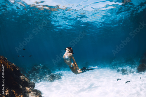 Freediver young woman with fins glides over sandy bottom with tropical fishes in transparent ocean © artifirsov
