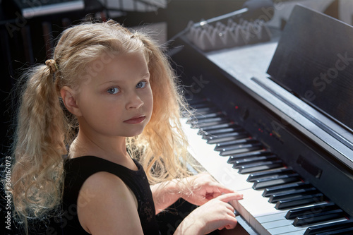 A blonde girl learns to play a musical instrument and looks at the camera.