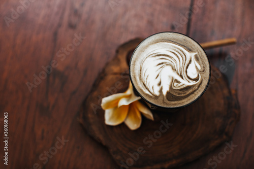Photo of glass of latte. Sanpshot of cup of coffee with milk, yellow flower on wooden table. Flat-lay