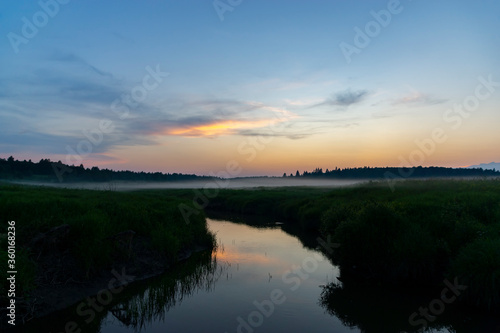 Nature at sunset. River and fog in the meadows. Forest on the horizon