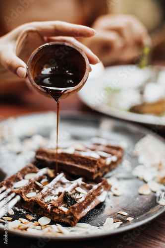 Food photo. Snapshot of maple syrup pouring on chocolate waffle with peanut and cream