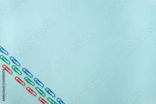 Blue, green and red paper clips located diagonally in the lower left corner of the photo. Horizontal photo. Flat lay minimalistic composition on a light blue background. Office supplies concept. Back photo