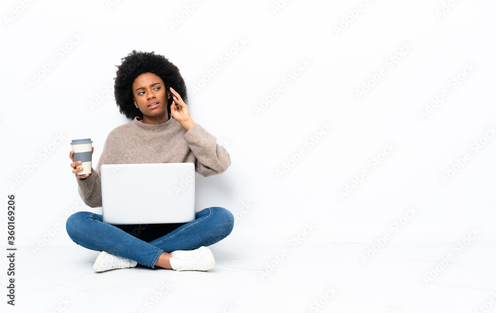 Young African American woman with a laptop sitting on the floor holding coffee to take away and a mobile Young African American woman with a laptop sitting on the floor holding coffee to take away and a mobile