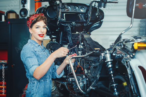 beautiful girl posing repairs a motorcycle in a workshop, pin-up style, service and sale