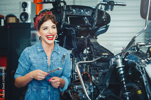 beautiful girl posing repairs a motorcycle in a workshop, pin-up style, service and sale