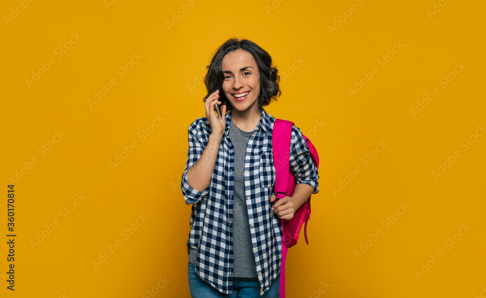 I'm on my phone! A young beautiful student, dressed casually, with her cute, pink backpack on her one shoulder, holding her smartphone in her hand by the ear, talking on the smartphone. I'm on my phone! A young beautiful student, dressed casually, with her cute, pink backpack on her one shoulder, holding her smartphone in her hand by the ear, talking on the smartphone.