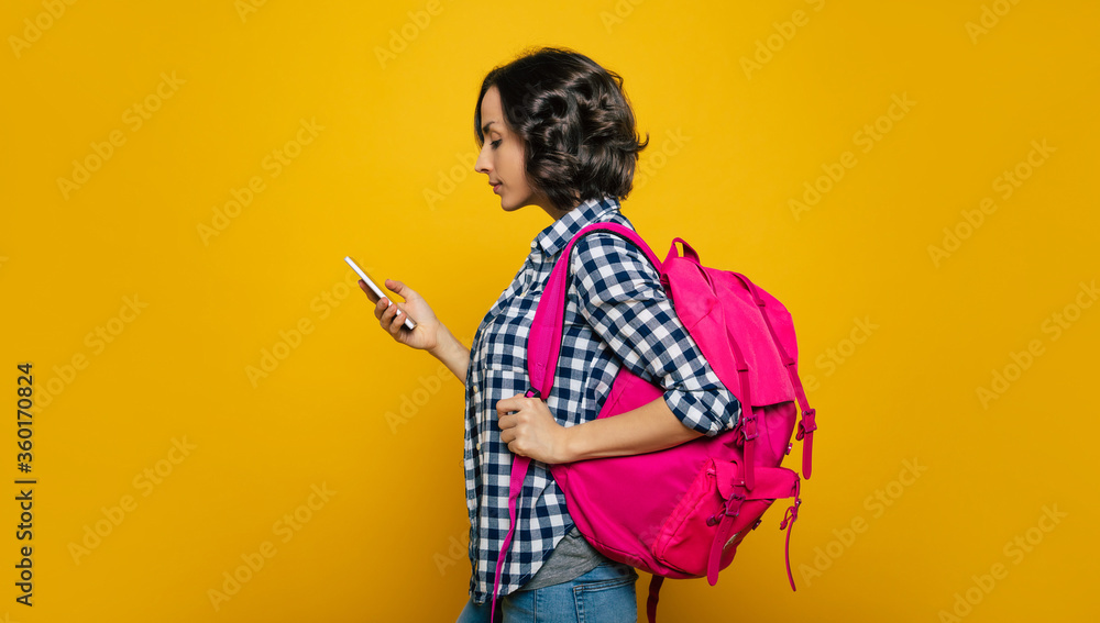Checking my schedule! A half-length photo of a young student, dressed casually, with her cute pink backpack on her one shoulder, turned sideways to check her schedule on her phone.