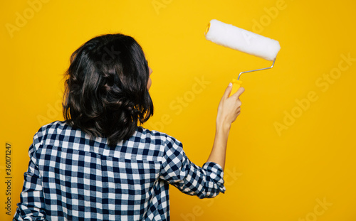 New color.. Close-up length photo of a nice back turned girl, in a black and white checkered shirt, holding a brush in her rigt hand, painting her wall. photo